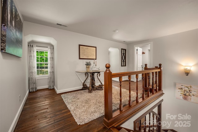 hallway with dark wood-style flooring, arched walkways, visible vents, and baseboards