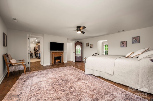 bedroom featuring a ceiling fan, dark wood-style flooring, baseboards, a walk in closet, and arched walkways