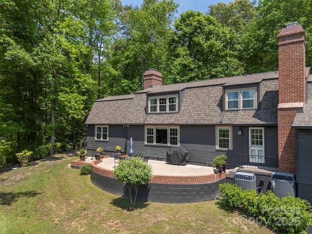 rear view of house featuring a yard, a chimney, a patio area, and roof with shingles