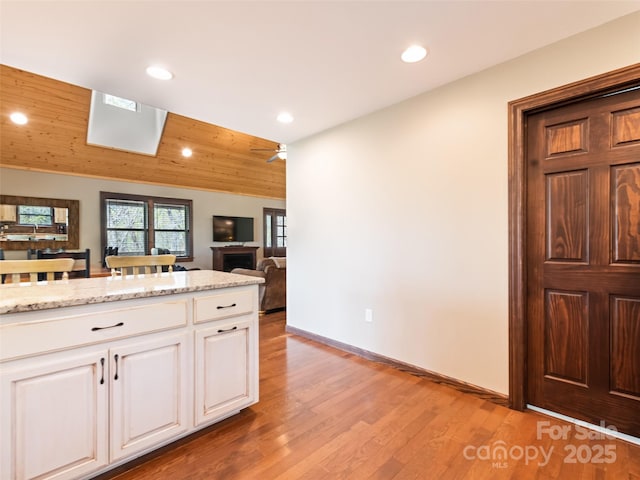 kitchen featuring white cabinets, recessed lighting, light stone counters, and light wood finished floors