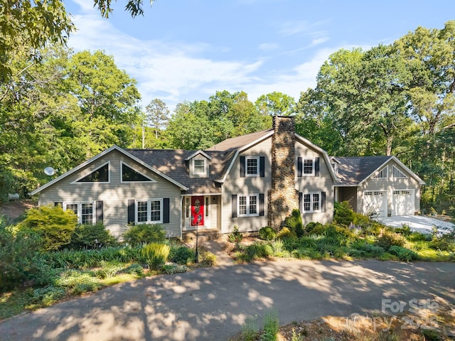 view of front of property with an attached garage, a chimney, driveway, and a gambrel roof