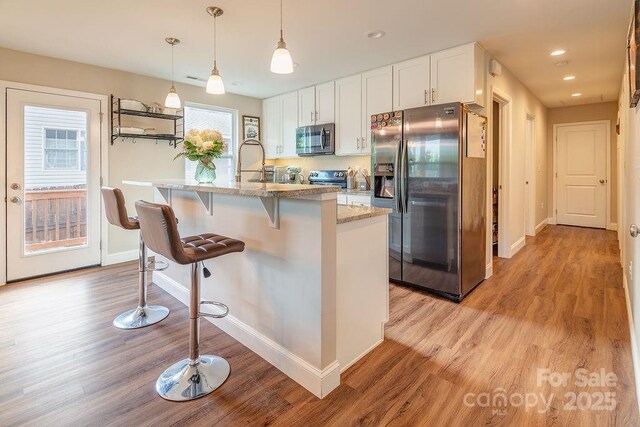 10 Half Moon Dr, Swannanoa, NC 28778 - kitchen with white cabinets, light wood-style floors, stainless steel appliances, baseboards, and a kitchen bar