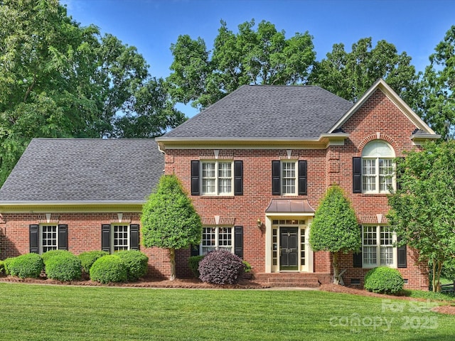 georgian-style home featuring a front yard, a shingled roof, and brick siding