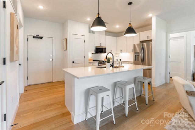 kitchen with appliances with stainless steel finishes, a sink, a breakfast bar area, light countertops, and light wood-type flooring