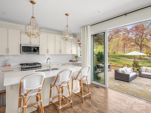 kitchen featuring light countertops, stainless steel appliances, a center island with sink, and a sink