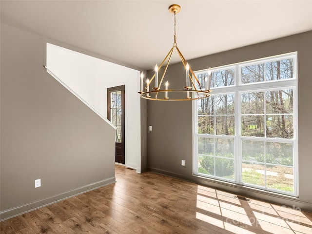 unfurnished dining area with baseboards, a chandelier, hardwood / wood-style floors, and visible vents