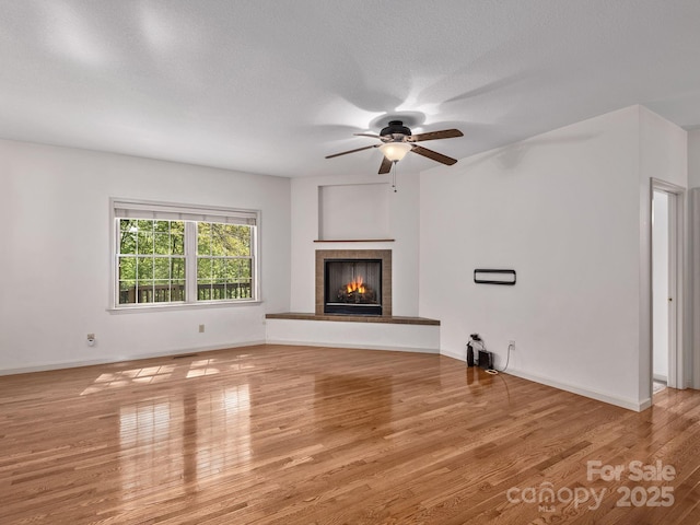 unfurnished living room featuring a tiled fireplace, baseboards, ceiling fan, and wood finished floors
