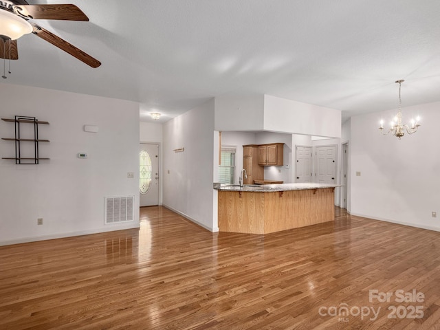 unfurnished living room featuring a sink, light wood-style flooring, ceiling fan with notable chandelier, baseboards, and visible vents