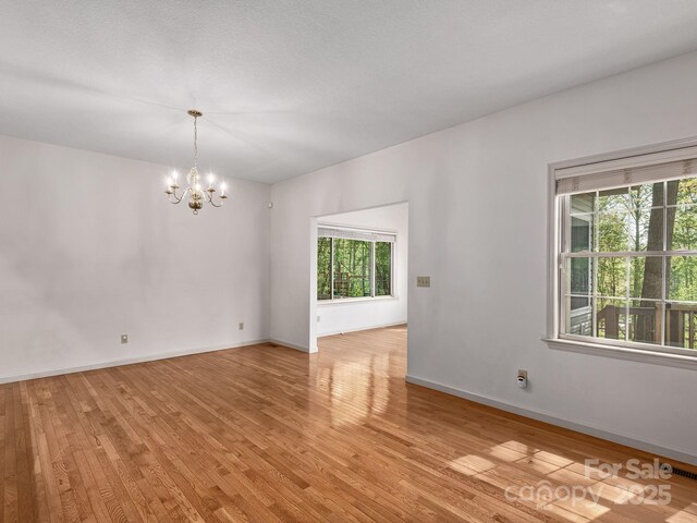 empty room featuring baseboards, a notable chandelier, visible vents, and light wood-style floors