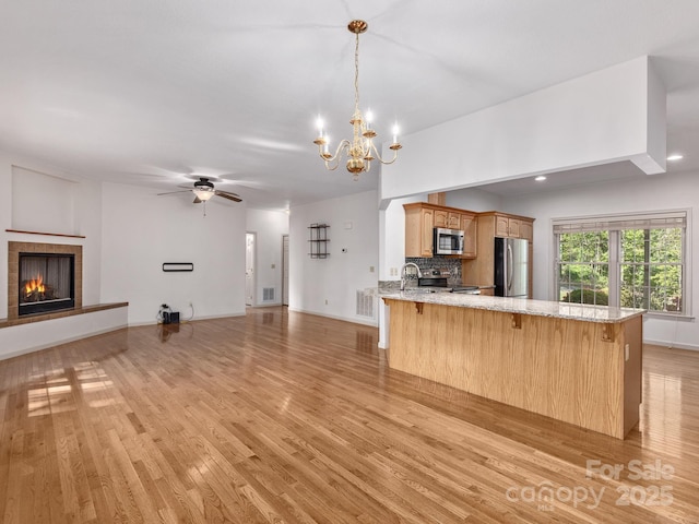 kitchen with a kitchen breakfast bar, a fireplace, open floor plan, light wood-style floors, and stainless steel appliances