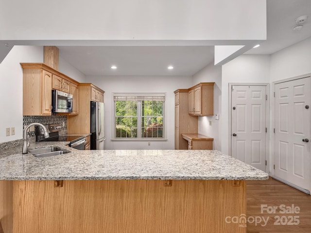 kitchen with a peninsula, wood finished floors, light stone countertops, a sink, and stainless steel appliances
