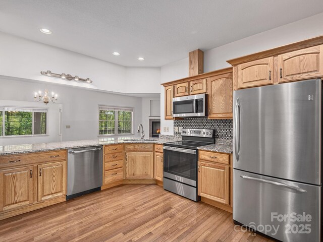 kitchen with light stone countertops, a sink, an inviting chandelier, stainless steel appliances, and light wood-style flooring