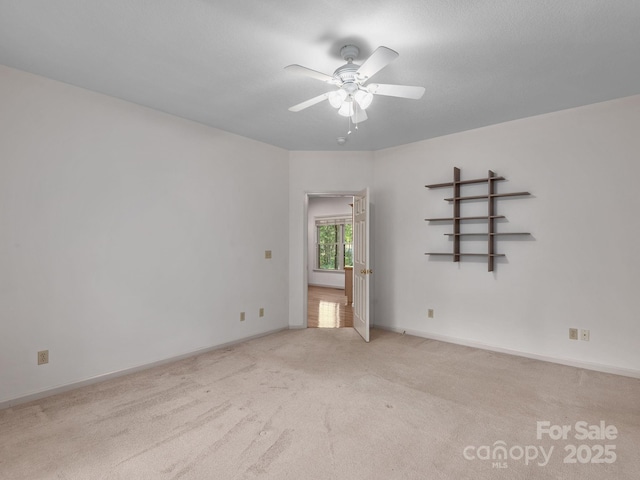 spare room featuring baseboards, a ceiling fan, and light colored carpet