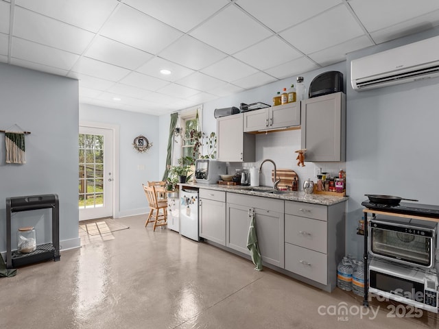 kitchen with an AC wall unit, white dishwasher, a paneled ceiling, and a sink