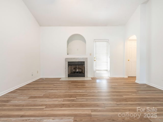 6212 Derryfield Dr, Charlotte, NC 28213 - unfurnished living room with a high end fireplace, light wood-style flooring, lofted ceiling, and arched walkways