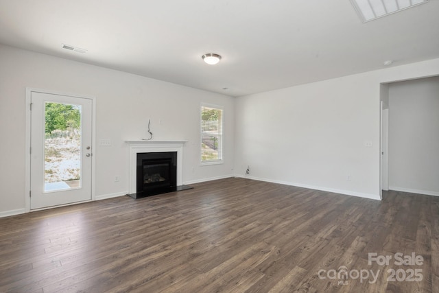 unfurnished living room with baseboards, a fireplace with raised hearth, dark wood-type flooring, and visible vents