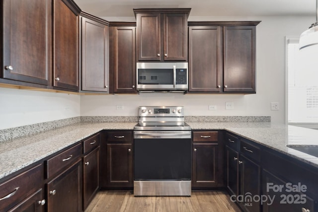 kitchen with dark brown cabinets, appliances with stainless steel finishes, light stone counters, and light wood finished floors