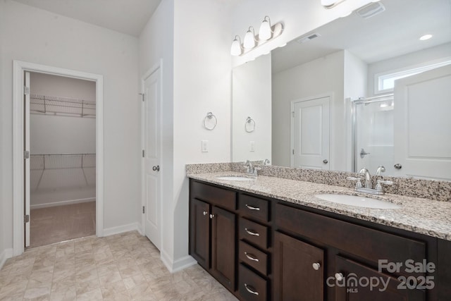full bath with double vanity, a sink, a stall shower, and a spacious closet