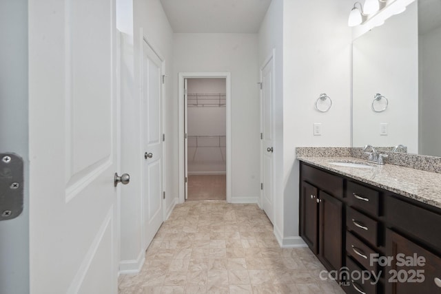 bathroom featuring vanity, baseboards, and a walk in closet
