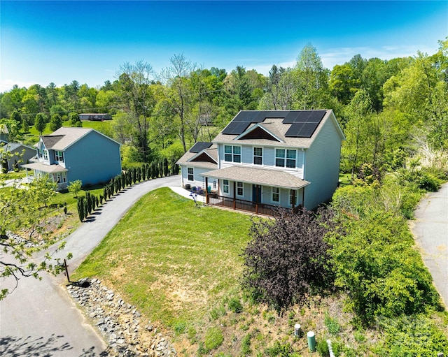 view of front of property with a porch, a front lawn, a wooded view, and solar panels