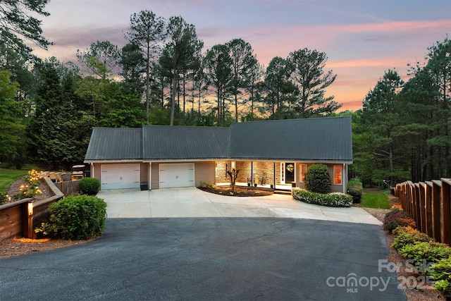 ranch-style house with concrete driveway, fence, metal roof, and a garage