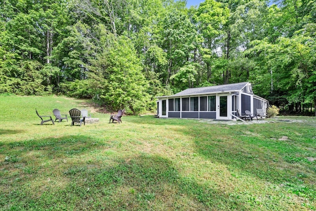 view of green lawn featuring a sunroom and a wooded view