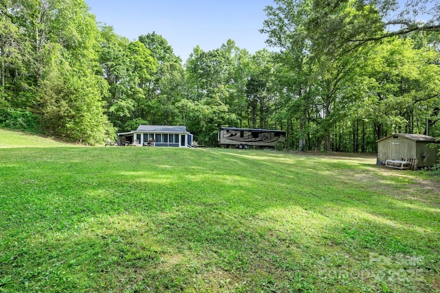 view of grassy yard featuring a shed, an outdoor structure, and a wooded view