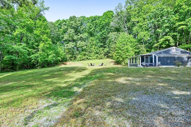 view of green lawn with a sunroom and a wooded view