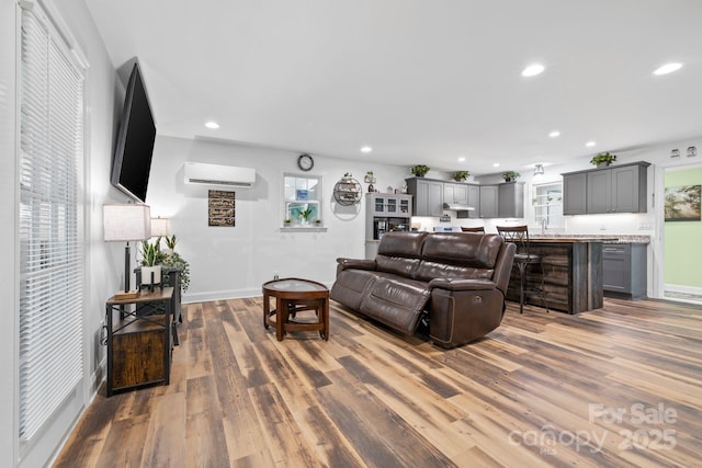 living room with an AC wall unit, wood finished floors, recessed lighting, and baseboards