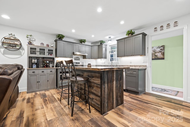 kitchen with gray cabinets, wood finished floors, a center island, a breakfast bar, and recessed lighting