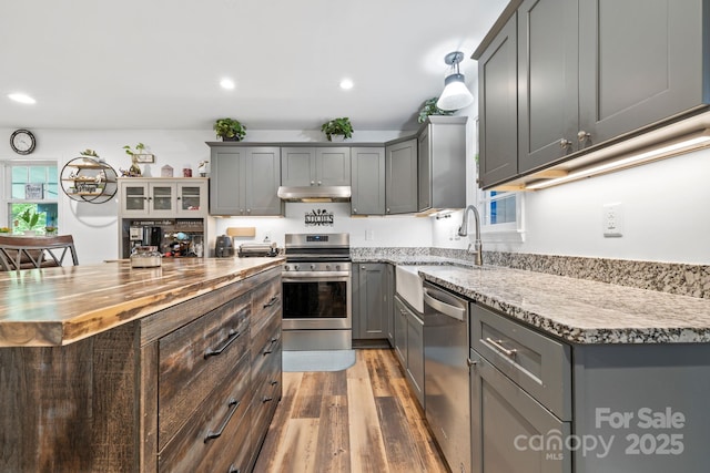kitchen with appliances with stainless steel finishes, gray cabinetry, butcher block counters, under cabinet range hood, and recessed lighting