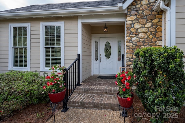 doorway to property with a shingled roof and stone siding