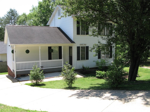 colonial-style house featuring a porch, a shingled roof, and a front lawn