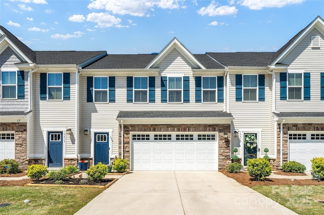 multi unit property featuring an attached garage, concrete driveway, and stone siding