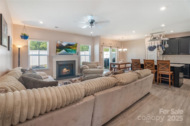 living room with visible vents, a glass covered fireplace, plenty of natural light, and ceiling fan with notable chandelier
