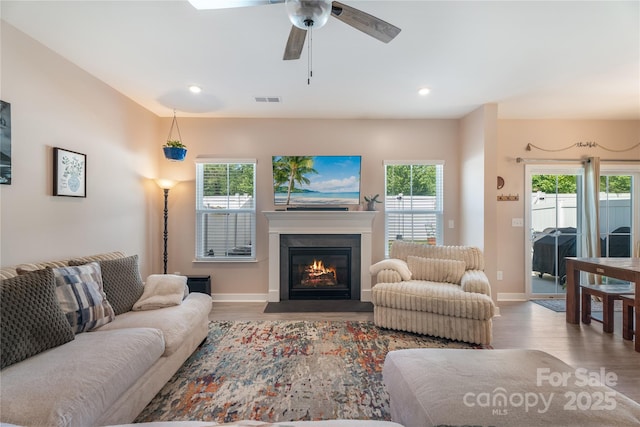 living area with ceiling fan, baseboards, a fireplace with flush hearth, wood finished floors, and visible vents