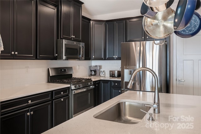 kitchen featuring backsplash, a sink, light stone counters, dark cabinets, and stainless steel appliances