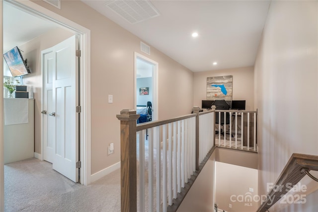 hallway with visible vents, baseboards, carpet floors, and an upstairs landing