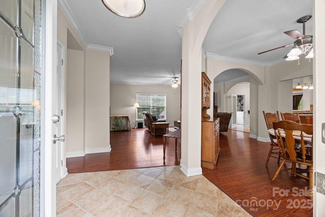 foyer with ceiling fan, arched walkways, crown molding, light wood-type flooring, and baseboards