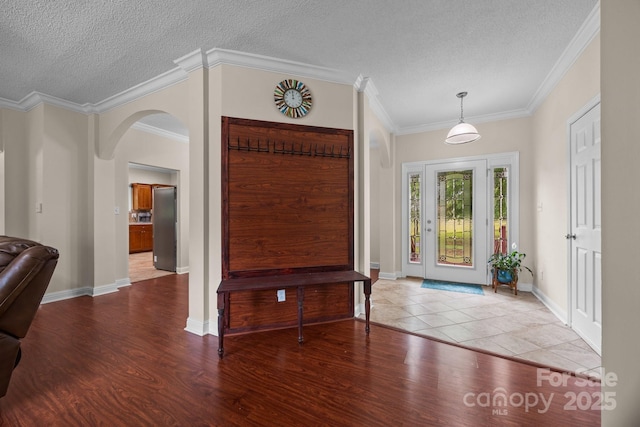entrance foyer featuring wood finished floors, arched walkways, a textured ceiling, crown molding, and baseboards