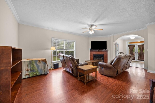 living room featuring arched walkways, ceiling fan, wood finished floors, a textured ceiling, and crown molding