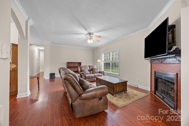 living room featuring a glass covered fireplace, a textured ceiling, ceiling fan, wood finished floors, and crown molding