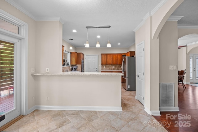 kitchen featuring appliances with stainless steel finishes, brown cabinets, a peninsula, arched walkways, and decorative backsplash