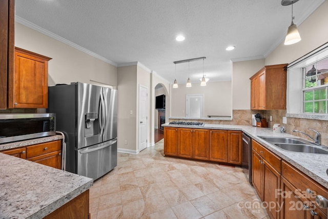 kitchen with stainless steel appliances, a sink, brown cabinets, ornamental molding, and arched walkways