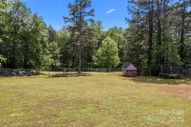 view of yard featuring a trampoline, a storage unit, a forest view, and an outbuilding