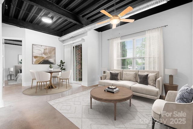 living area featuring finished concrete flooring, baseboards, and ceiling fan