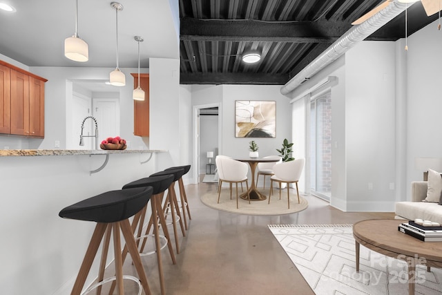 kitchen with concrete flooring, brown cabinets, a breakfast bar area, baseboards, and a sink
