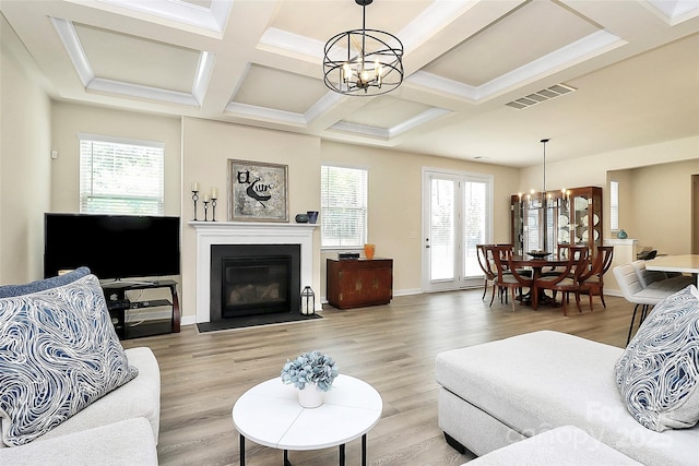 living area with visible vents, a chandelier, coffered ceiling, a fireplace with flush hearth, and light wood-style flooring
