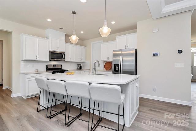 kitchen with a breakfast bar area, appliances with stainless steel finishes, a center island with sink, a sink, and light wood-style flooring