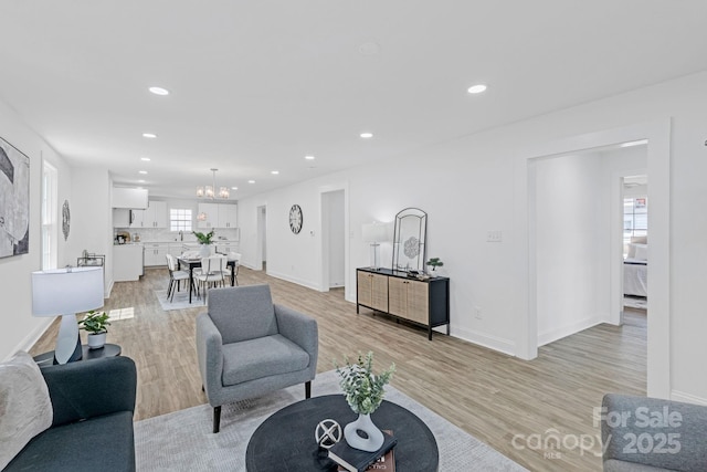 living area with baseboards, light wood finished floors, recessed lighting, and a chandelier